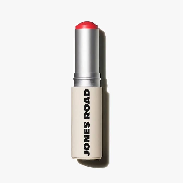 A tube of JONES ROAD lipstick with a beige base and silver body, featuring a vibrant bright red shade. The brand name JONES ROAD is printed vertically in bold black letters on the tube, perfect for those who love brights.