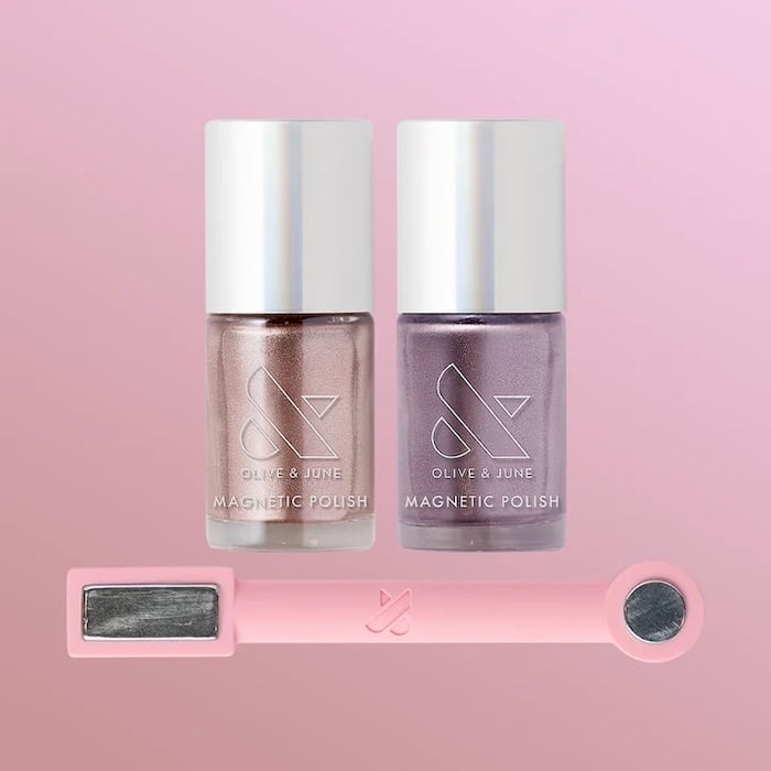 Two bottles of Olive & June magnetic nail polish—one rose gold, one lavender—stand side by side on a pink background, with a pink magnetic tool below them, perfect for trying out summer nails and the latest manicure trends.
