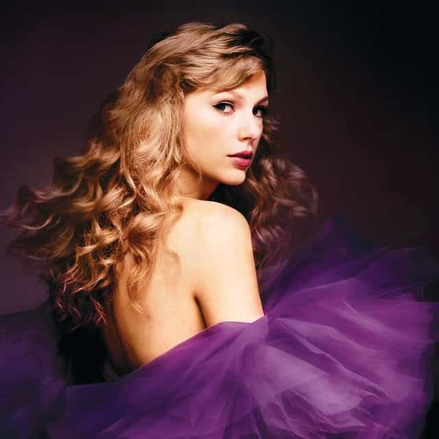 A woman with long, wavy blonde hair looks over her shoulder, evoking the mystique of Taylor Swift Vault Tracks. She wears a strapless gown of voluminous purple tulle against a dark background that makes her and the dress stand out.