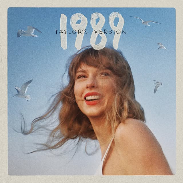 A woman with wavy hair and red lipstick smiles against a blue sky with seagulls. The text above her reads 1989 Taylor’s Version, celebrating Taylor Swift and the excitement of Vault Tracks in a soft, vintage style.