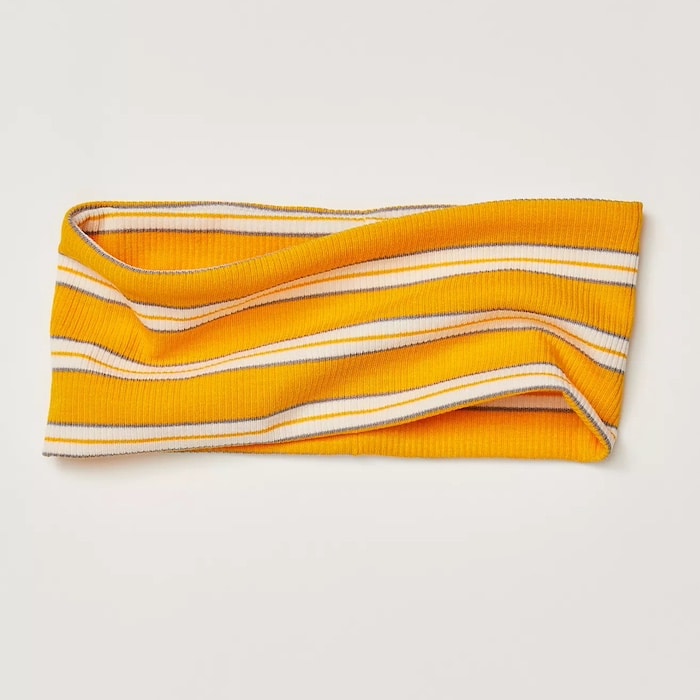 A vibrant summer hair accessory, this yellow, white, and orange ribbed knit headband features horizontal stripes and is laid flat on a light background.