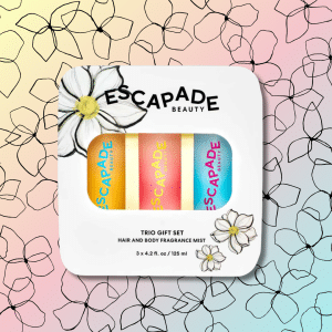 A pastel-colored Escapade Beauty trio gift set with three fragrance mists is displayed on a floral, gradient background. The packaging has a flower illustration and the text ESCAPADE BEAUTY TRIO GIFT SET.