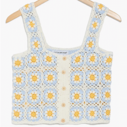 A sleeveless crochet crop top with a square pattern in pastel blue and cream, featuring yellow flower motifs and front buttons—perfect for summer outfits or The Summer I Turned Pretty inspired outfits. Displayed on a wooden hanger against a white background.