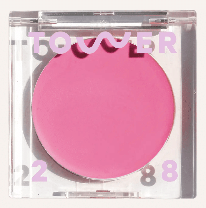 A square, clear plastic compact containing a bright pink cream blush. The lid displays the brand name Tower 28 in bold, light purple letters—perfect to bring on the brights to your makeup routine.