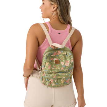 A woman wearing a pink tank top and beige shorts is shown from the back, carrying a small green floral backpack with beige straps. Her wavy hair and casual outfit evoke the effortless summer style of The Summer I Turned Pretty.